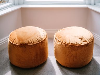 Two round orange ottomans on gray carpet in a corner with windows at Craig Cottage in Bowness-On-Windermere