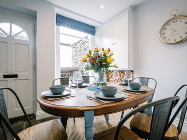 A dining area with a wooden table set for four with bowls plates glasses and a flower vase at Craig Cottage Bowness-On-Windermere