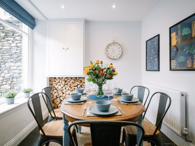 A dining room with a wooden table set with blue bowls and plates surrounded by metal chairs and a vase of flowers at Craig Cottage in Bowness-On-Windermere