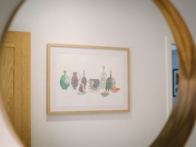 A framed abstract artwork of vases on a white wall seen through a round mirror at Craig Cottage in Bowness-On-Windermere