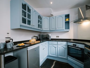 A kitchen with light blue cabinets black countertop a microwave oven and a stove at Craig Cottage in Bowness-On-Windermere