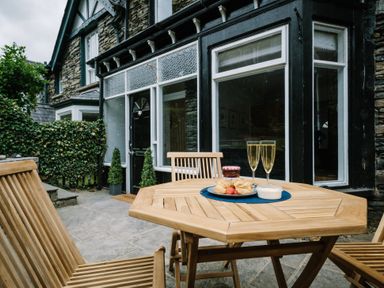 A wooden outdoor table with two glasses of champagne and a plate of scones in front of a stone house at Craig Cottage in Bowness-On-Windermere