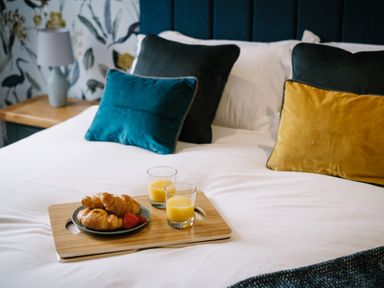 A bed with pillows and a wooden tray holding croissants strawberries and two glasses of orange juice at Craig Cottage in Bowness-On-Windermere