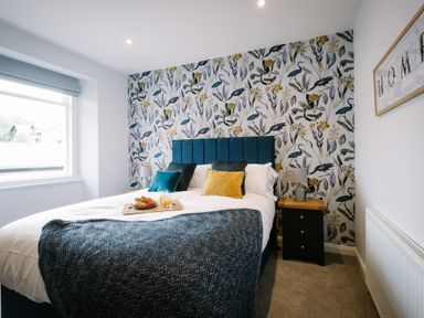 A bedroom with a bed with pillows and a tray on it bedside tables with lamps and a window at Craig Cottage in Bowness-On-Windermere