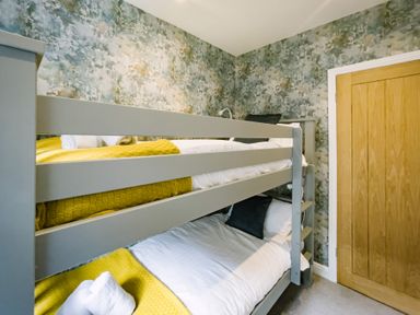 A bedroom with grey bunk beds yellow blankets and a wooden door at Craig Cottage in Bowness-On-Windermere