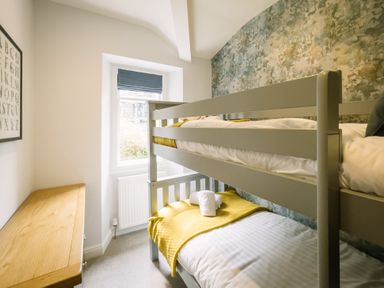 A small bedroom with a bunk bed wooden dresser and window at Craig Cottage in Bowness-On-Windermere