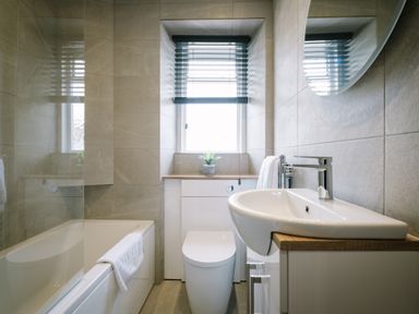 A bathroom with a bathtub a toilet a sink a window with blinds and a small plant on the windowsill at Craig Cottage in Bowness-On-Windermere