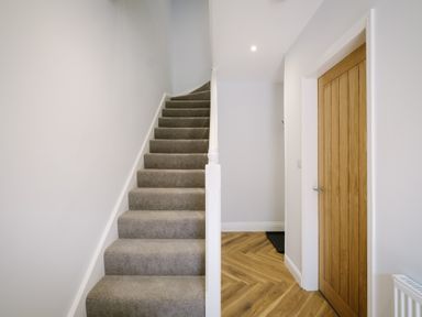 A hallway with carpeted stairs and a wooden door with white walls and wooden floor at Craig Cottage in Bowness-On-Windermere