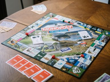 A Monopoly board game set up on a wooden table with cards dice and money at Craig Cottage in Bowness-On-Windermere