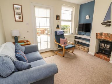A living room with a blue sofa and chair a fireplace and wall-mounted tv at 9 Harefield Cottages in Lympstone