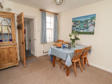 A dining room with a table set with cups and a vase of flowers and wooden chairs at 9 Harefield Cottages in Lympstone