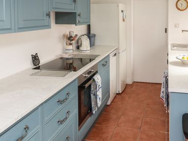 A kitchen with blue cabinets white countertops a white refrigerator and a clock on the wall at 9 Harefield Cottages in Lympstone