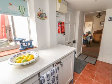 A kitchen counter with a bowl of fruit and a blue scale near a window overlooking a door with fire safety equipment at 9 Harefield Cottages in Lympstone