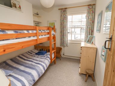 A bedroom with a wooden bunk bed a chest of drawers a window with floral curtains and a small stool at 9 Harefield Cottages Lympstone