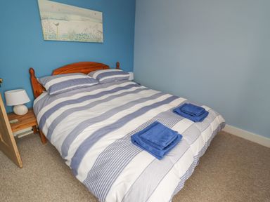 A bedroom with a double bed with striped bedding and two folded blue towels at 9 Harefield Cottages in Lympstone