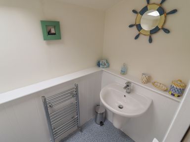 A bathroom corner with a white sink a towel rack a small trash can and decorative items on the shelf at 9 Harefield Cottages in Lympstone