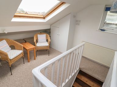 A small seating area with two wicker chairs and a wooden table under a skylight at 9 Harefield Cottages in Lympstone
