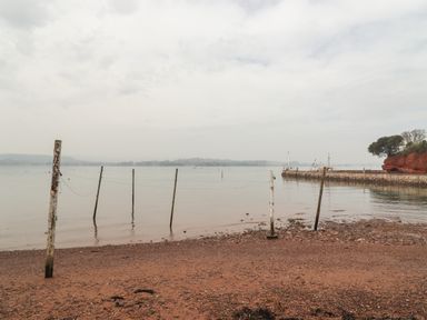 A beach with wooden poles connected by wires and a stone pier extending into calm water at 9 Harefield Cottages in Lympstone
