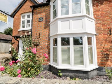 Exterior view of a brick cottage with white bay windows and pink flowers in front at Oakapple Cottage Swan Green near Lyndhurst