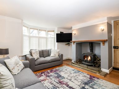 A living room with two grey sofas near a bay window and a fireplace with a wood stove at Oakapple Cottage in Swan Green near Lyndhurst