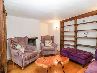 A sitting area with two striped armchairs purple ottoman wooden coffee table and wall shelves at Oakapple Cottage Swan Green near Lyndhurst