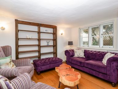A living room with purple sofa striped armchairs wooden coffee table and wooden shelves at Oakapple Cottage Swan Green near Lyndhurst