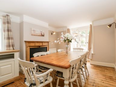 A dining room with a wooden table and chairs a fireplace and a vase with flowers on the table at Oakapple Cottage in Swan Green near Lyndhurst