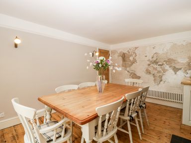 A dining room with a wooden table and six white chairs a vase with flowers on the table and a world map on the wall at Oakapple Cottage in Swan Green near Lyndhurst