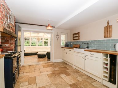 A kitchen with white cabinets wooden countertops a brick oven wall and a seating area visible through a doorway at Oakapple Cottage Swan Green near Lyndhurst