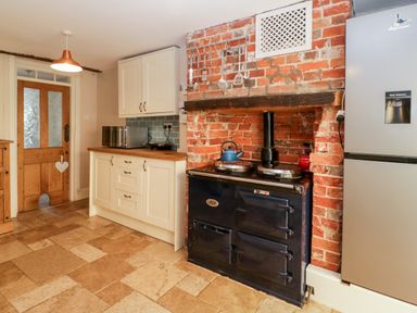 A kitchen with a wood door a microwave on a countertop a blue stove set into a brick wall and a silver refrigerator at Oakapple Cottage Swan Green near Lyndhurst