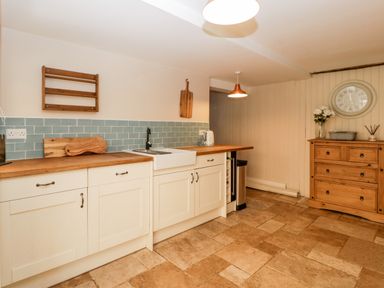 A kitchen with white cabinets wooden countertops a sink a wooden dresser a wall clock and a pendant light at Oakapple Cottage Swan Green near Lyndhurst