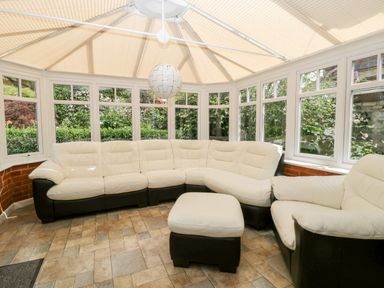 A conservatory with a sectional sofa, an armchair, and an ottoman with windows showing greenery outside at Oakapple Cottage in Swan Green near Lyndhurst