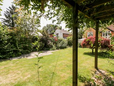 A garden with grass lawn trees and shrubs viewed from under a wooden pergola at Oakapple Cottage in Swan Green near Lyndhurst