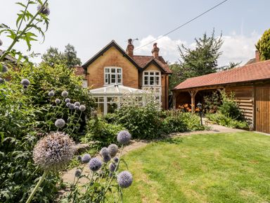 A garden with flowering plants and a lawn in front of a brick house and a wooden garage at Oakapple Cottage Swan Green near Lyndhurst