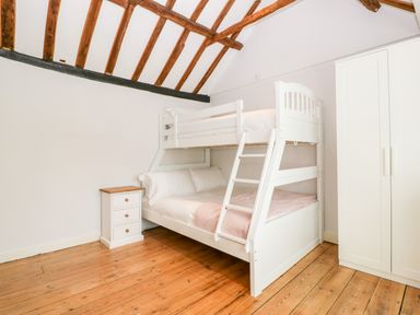 A bedroom with a white bunk bed a bedside table and a wardrobe with exposed wooden beams on the ceiling at Oakapple Cottage in Swan Green near Lyndhurst
