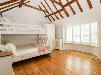 A bedroom with wooden floor a bunk bed a wardrobe and a bay window with shutters at Oakapple Cottage Swan Green near Lyndhurst