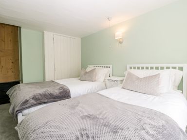 A bedroom with two single beds each with pillows and gray blankets at Oakapple Cottage in Swan Green near Lyndhurst