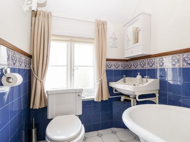 A bathroom with a toilet sink bathtub beige curtains and blue tiles at Oakapple Cottage in Swan Green near Lyndhurst