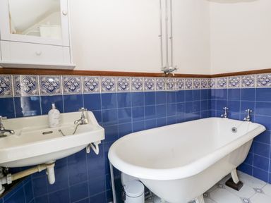 A bathroom with a white clawfoot bathtub and a wall-mounted sink with blue tiled walls at Oakapple Cottage in Swan Green near Lyndhurst