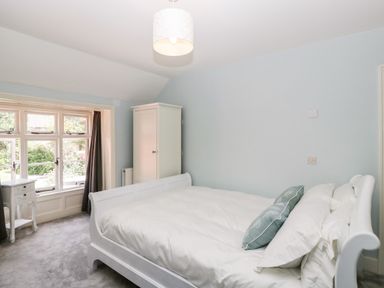 A bedroom with a white bed white wardrobe white nightstand and a window with curtains at Oakapple Cottage in Swan Green near Lyndhurst