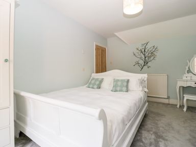 A bedroom with a white bed and green pillows a wooden door and a white vanity table with a mirror at Oakapple Cottage in Swan Green near Lyndhurst