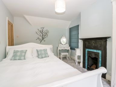 A bedroom with a white bed two green pillows a black fireplace and a white dressing table with a mirror at Oakapple Cottage in Swan Green near Lyndhurst