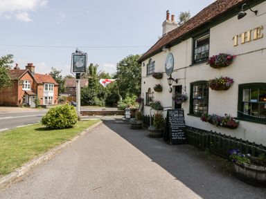 An exterior view of a pub with flower baskets and a sign near a road at Oakapple Cottage Swan Green near Lyndhurst