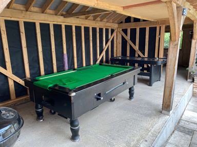 A covered outdoor area with a pool table and air hockey table on a concrete floor at Oakapple Cottage in Swan Green near Lyndhurst