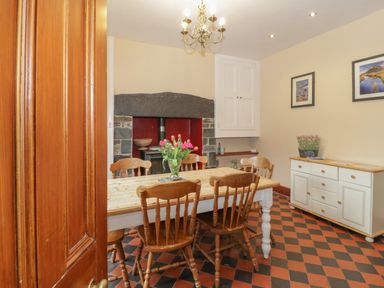 A dining room with wooden table and chairs flowers on table fireplace and cabinet at Ty Capel in Betws-Y-Coed