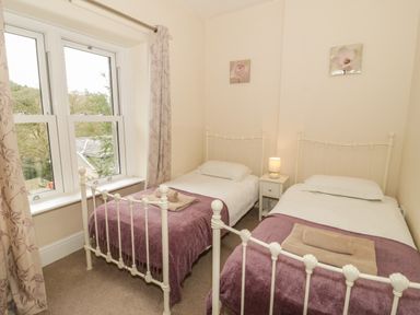 A bedroom with two single metal beds blankets and towels bedside table with lamp and a window at Ty Capel in Betws-Y-Coed