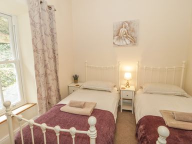 A bedroom with two single beds purple blankets bedside tables and a window with curtains at Ty Capel in Betws Y Coed