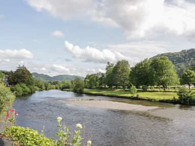 A river with green trees and hills in the background at Ty Capel in Betws-Y-Coed