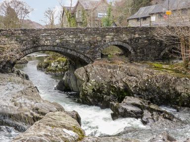 A stone bridge over a river with rocks and buildings in the background at Ty Capel in Betws Y Coed