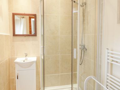 A bathroom with a shower enclosure a sink with a mirror above and a towel radiator at Ty Capel in Betws-Y-Coed